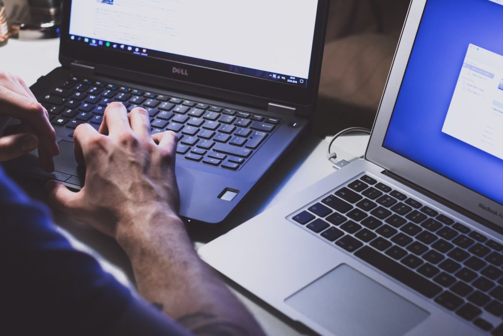 man's hands working on two laptops